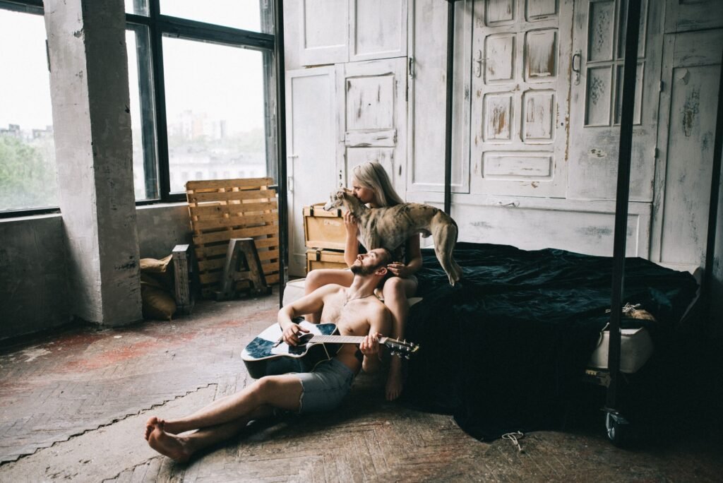 Young couple with a dog in a cozy bedroom, enjoying music on an acoustic guitar.